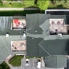 Aerial view of a building roof with three rooftop patios, each furnished with tables, chairs, and umbrellas.