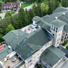 Aerial view of a multi-story residential building with green roofs, surrounded by trees and parked cars.